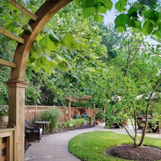 A serene garden with a curved pathway and wooden archway surrounded by lush greenery.