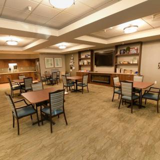 A spacious dining area with several tables and chairs, featuring wood flooring, warm lighting, a television, and bookshelves along the walls.