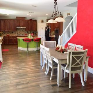 A spacious open-concept kitchen and dining area with wood flooring, featuring a bold red accent wall and elegant chandelier.