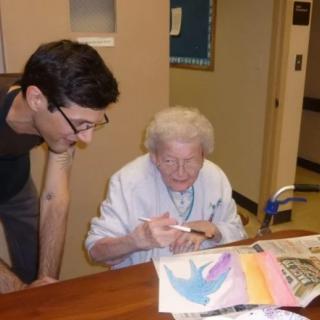 An elderly woman engaging in painting with the assistance of a young person.