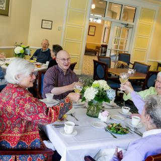 A group of seniors enjoying a meal and toasting together in a dining room.