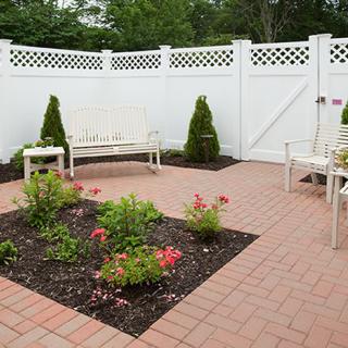 A cozy patio with white fencing, featuring benches and a small flower garden.