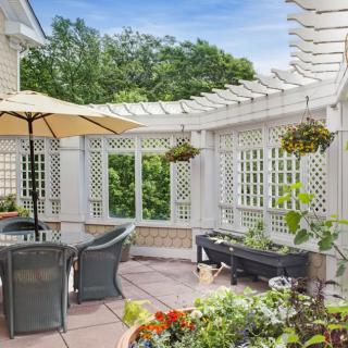 A cozy outdoor patio with a pergola, seating area, and lush greenery.