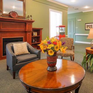 A cozy living room with a fireplace, featuring comfortable seating and a vase of vibrant flowers on the table.