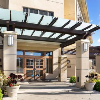 Modern building entrance with a glass canopy and landscaping.