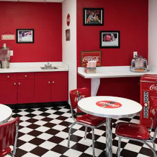 A vibrant retro diner with red walls and a classic black-and-white checkered floor, featuring small tables and metal chairs.