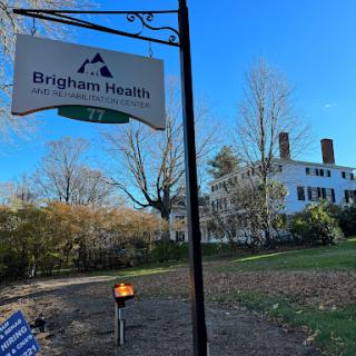 A sign for Brigham Health with a historic building in the background under a clear blue sky.