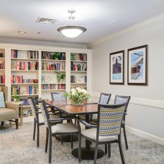 A cozy dining area with a wooden table and chairs, surrounded by bookshelves and decorated with artwork on the walls.