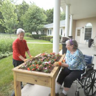 Two women engage in gardening activities, creating a vibrant flower bed together.