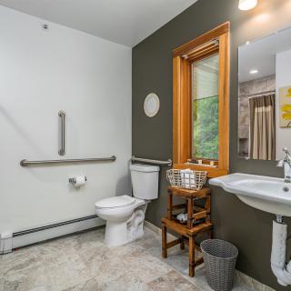 A modern, accessible bathroom with grab bars, toilet, sink, and a window.