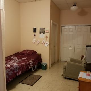 A small bedroom with a single bed, a chair, and a desk, featuring wall decorations and a closet.