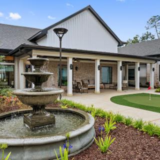 A serene outdoor area featuring a decorative fountain, landscaped gardens, and a welcoming residential architecture.