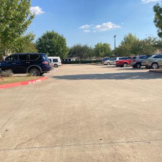 A view of a parking lot filled with various cars, surrounded by trees under a clear blue sky.