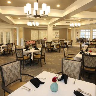An elegant dining room with neatly arranged tables and chairs, adorned by chandeliers.