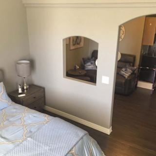 A cozy bedroom with a neatly made bed, nightstand with lamp, and decorative mirror on the wall.