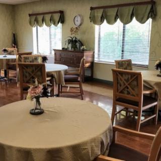 A cozy dining area with round tables, wooden chairs, and decorative curtains.