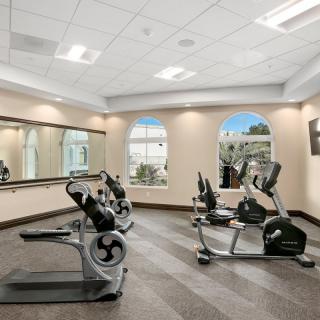 A well-lit gym featuring treadmills and exercise bikes, with large mirrors on the wall.