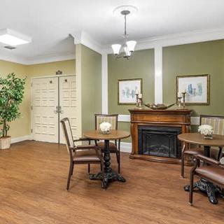 A cozy dining area with a fireplace, wooden tables and chairs, decorated with plants and artwork on the walls.