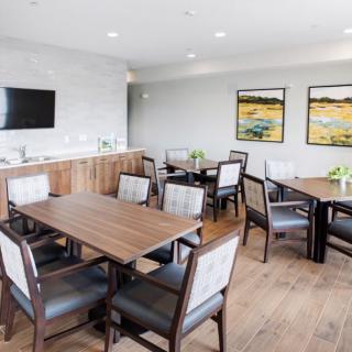 A modern meeting room with multiple tables and chairs, a television mounted on the wall, and artwork displayed.