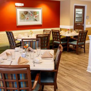 A cozy restaurant dining area with neatly set tables and chairs, featuring warm lighting and elegant decor.
