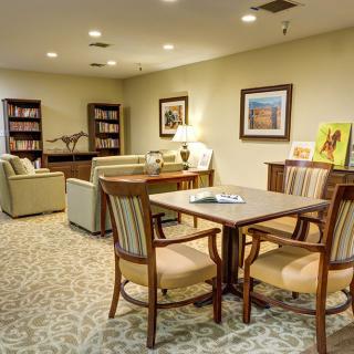 A cozy living room with a table, chairs, sofas, bookshelves, and artwork on the walls.