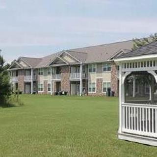 A row of apartment buildings with a grassy lawn and a white gazebo in the foreground.
