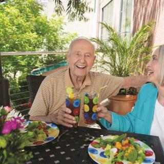 An elderly couple enjoying drinks and salads together in a garden setting.
