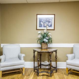 A waiting room with two armchairs, a wooden table, and a framed painting on the wall.
