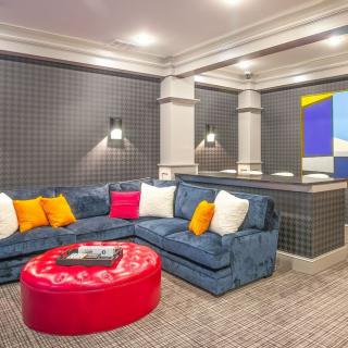 A stylish living room featuring a blue sectional sofa with colorful pillows, a red ottoman, and modern wall art.