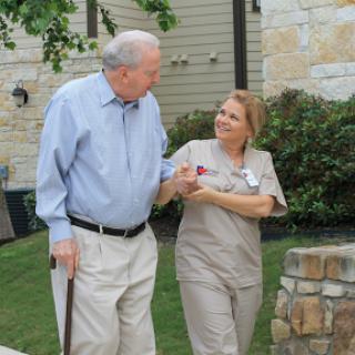 A caregiver assists an elderly man while they enjoy a stroll outdoors.