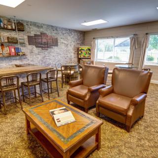 A cozy living room with leather armchairs, a wooden coffee table, and a bookshelf against a brick accent wall.