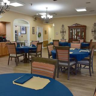 A spacious dining room with multiple tables covered in blue tablecloths, surrounded by wooden chairs and decorated with chandeliers.