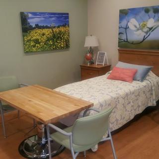 A cozy hospital room with a single bed, colorful artwork, and simple furniture.