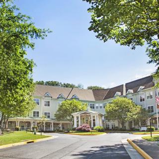 A large, elegant residential building with trees and a driveway under a clear sky.