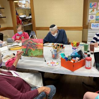A group of seniors engaged in an art class, painting while wearing masks.