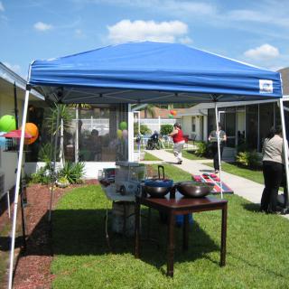 A backyard gathering under a blue canopy tent on a sunny day.