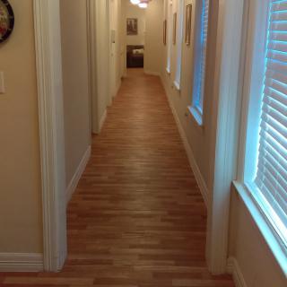 A well-lit hallway with wooden flooring and windows along one side.