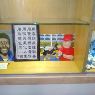 A collection of artworks displayed on a shelf, featuring portraits and an illustration of a person with a dog.