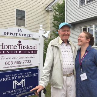 A caregiver and an elderly man standing outside a senior care facility.