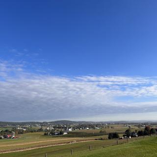 A picturesque rural landscape under a clear blue sky with scattered clouds.