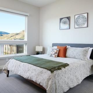 A bright and cozy bedroom with a neatly made bed, decorative pillows, and two framed artworks on the wall, featuring a window view of a scenic landscape.