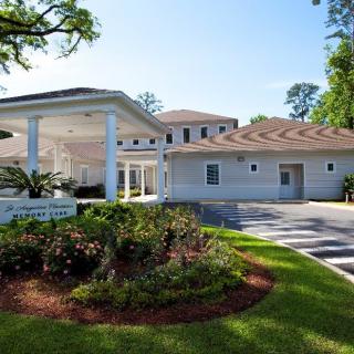 A spacious white building with well-maintained landscaping and a driveway, surrounded by trees.