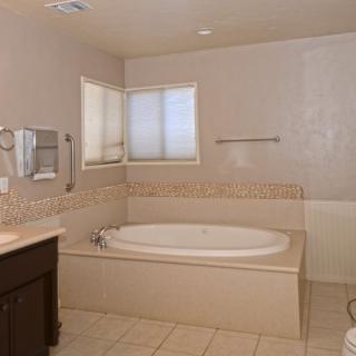 A spacious bathroom featuring a large bathtub, a sink with a mirror, and tiled flooring.