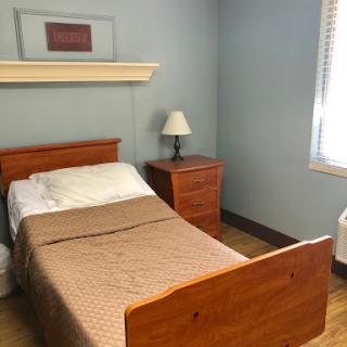 A simple and tidy bedroom featuring a single wooden bed, nightstand, and lamp against blue walls.