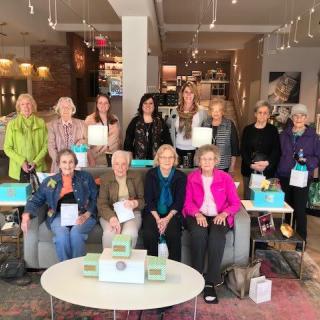 A group of women gathered indoors, seated and standing, in a casual setting.