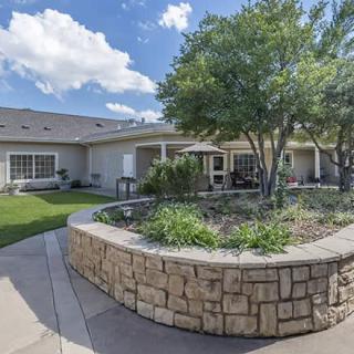 A well-maintained garden area with a stone border and patio in front of a residential building.
