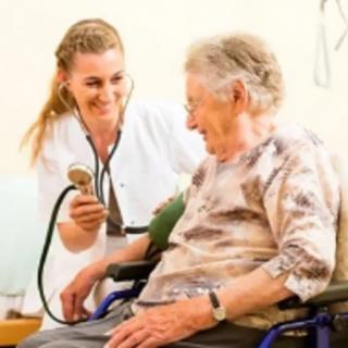 A nurse checking the blood pressure of an elderly person in a wheelchair.