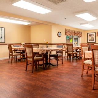 An empty dining area with wooden floors, arranged tables and chairs, and warm lighting.
