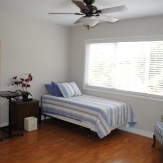 A minimalist bedroom with a single bed and striped bedding, brightened by natural light from a large window.