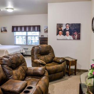 A cozy living space featuring recliner chairs, wall art, and a window with curtains, leading into a bedroom area.